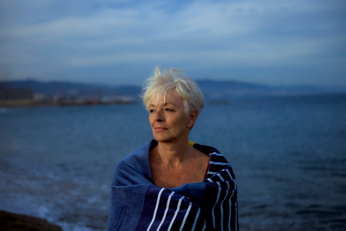 Older woman wrapped in striped towel by the sea for ERGO lifestyle insurance campaign