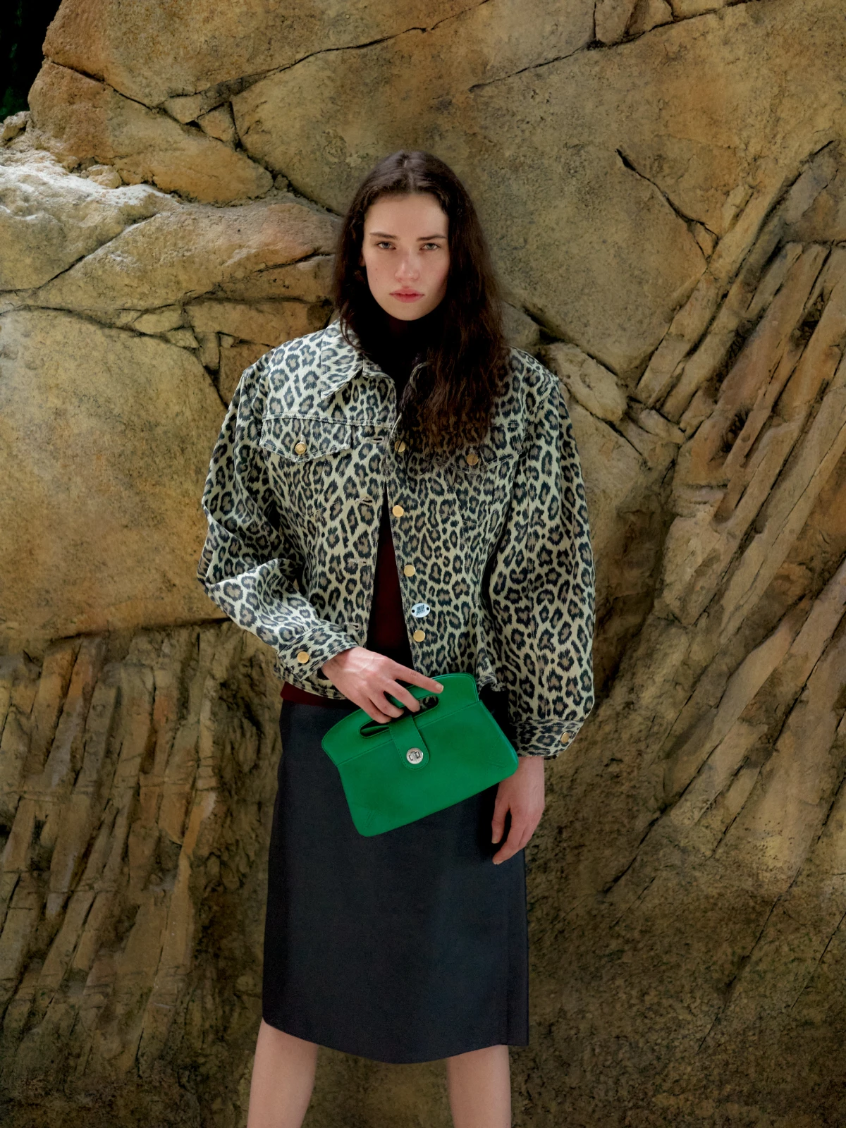 Woman holding green handbag against rocky landscape for Material Girl fashion advertorial campaign