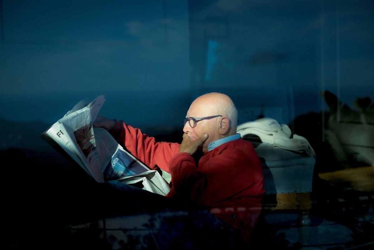 Bald man reading newspaper through window reflection indoors for ERGO insurance campaign